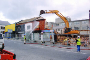 Market Place Lisburn renovations taking place June 2005, workers demolishing shop fronts with digger.